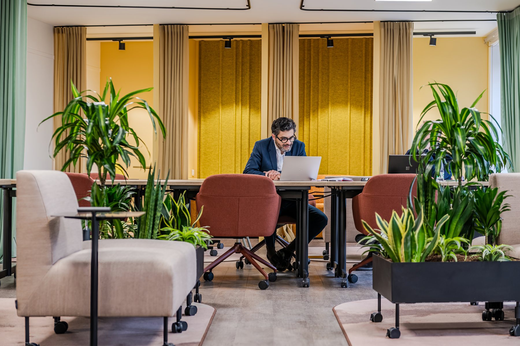 Le plateau ouvert des Ateliers Lill'loi en activité : un utilisateur au travail entre alcôves à rideaux jaunes et végétalisation abondante.